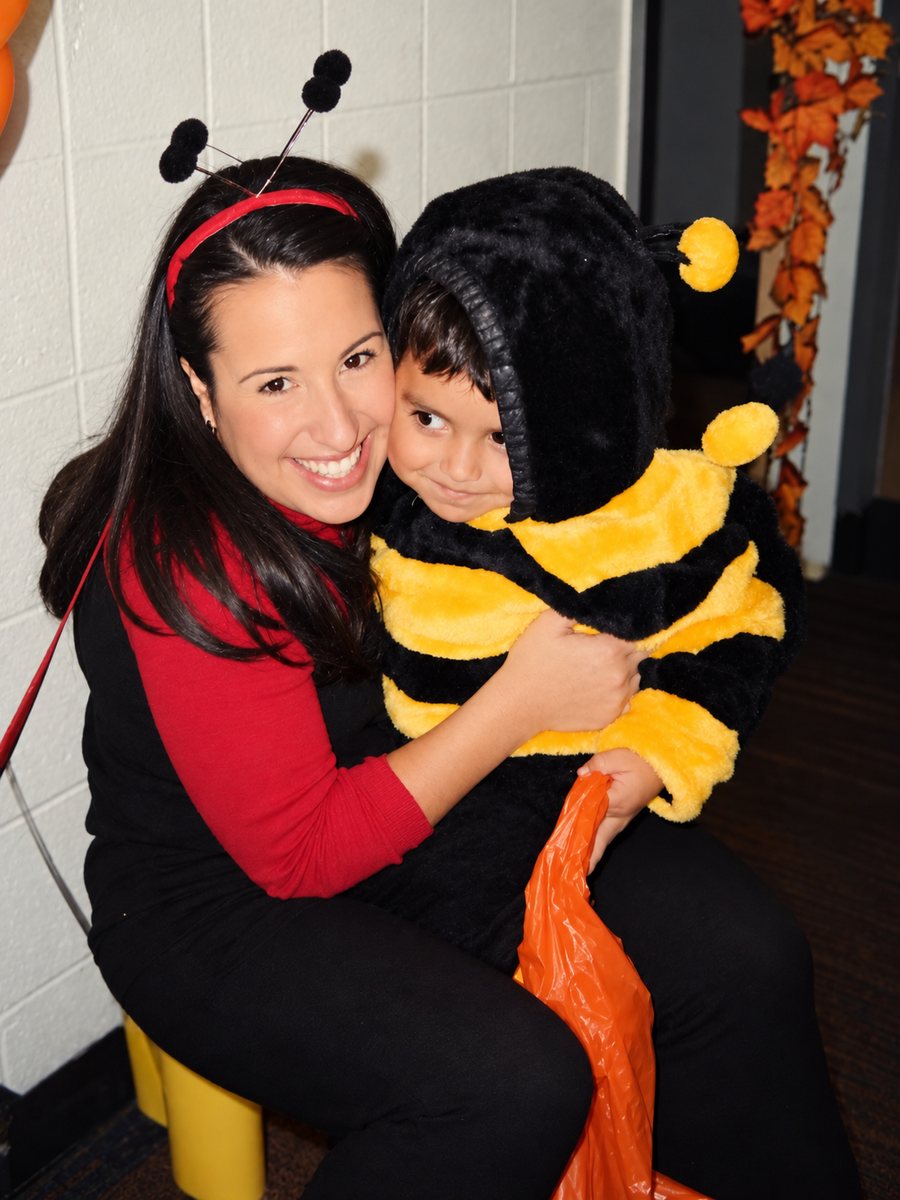 A young Jennifer in ladybug antennae hugging a smiling little boy in a bumblebee costume at a Halloween party